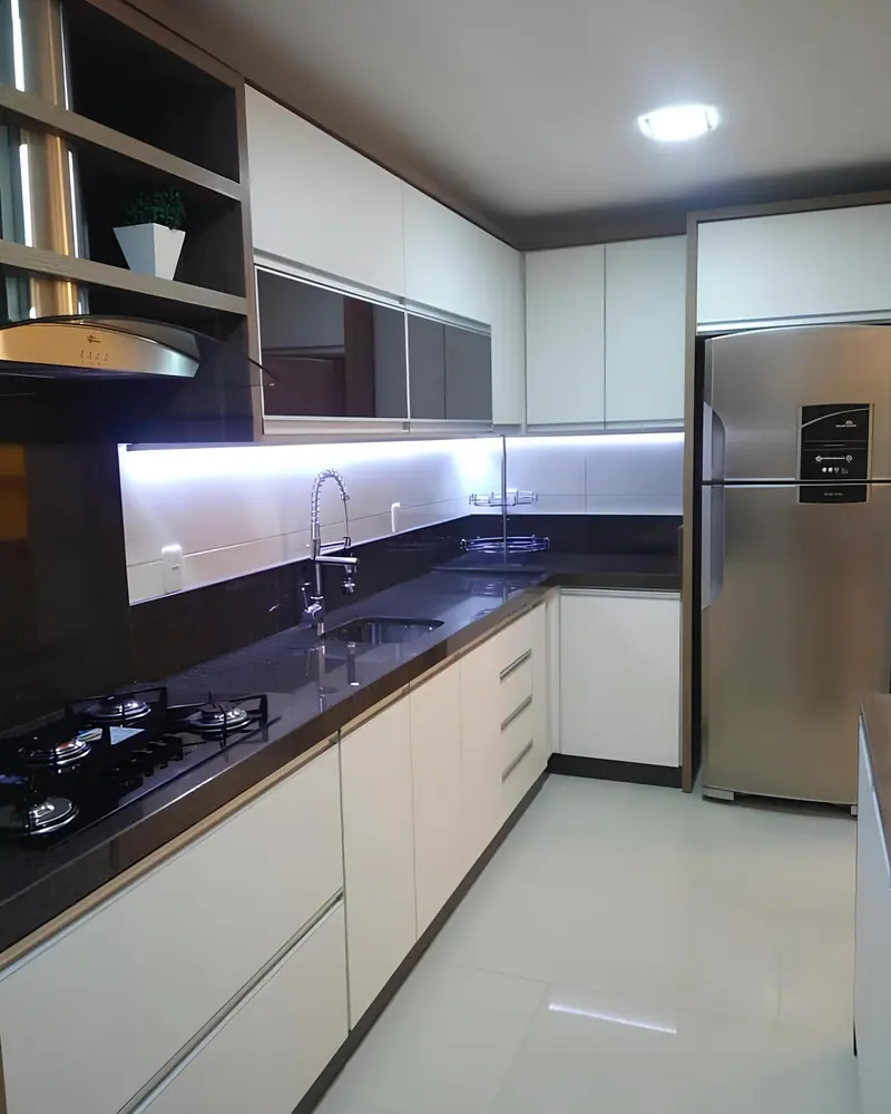 Cozinha em L com armários brancos, bancada de granito preto e iluminação de LED sob os armários superiores