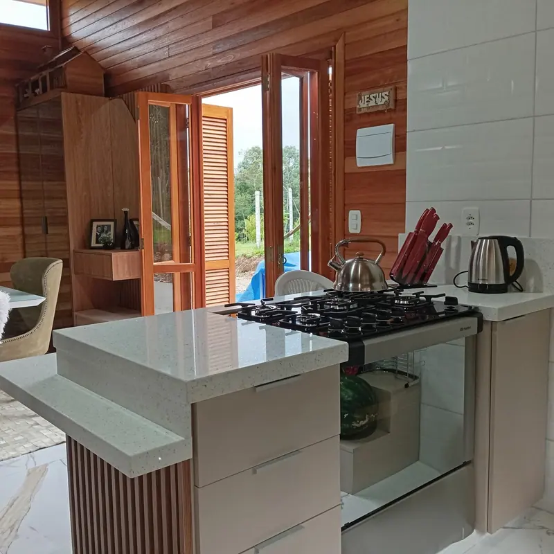 Cozinha sob medida em casa de madeira, com bancada clara, fogão de embutir e base ripada