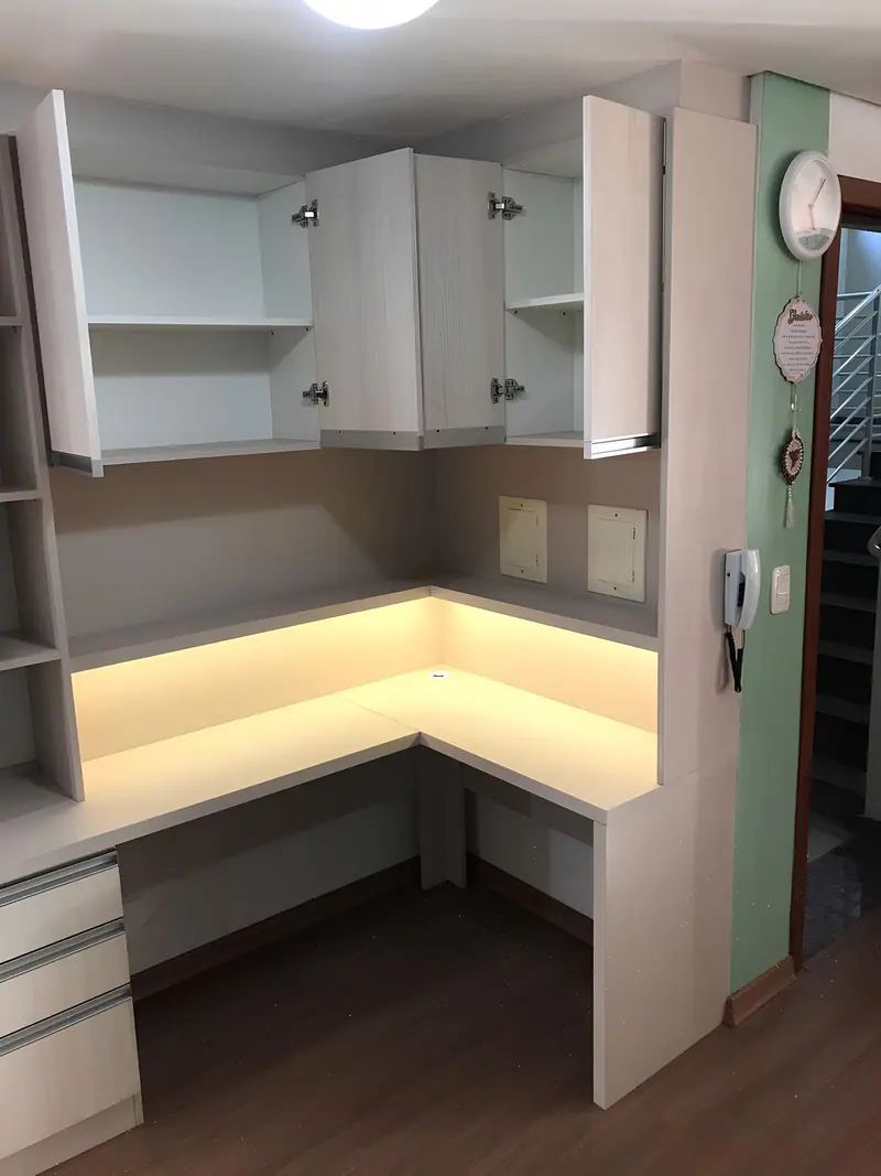 Home office em L com bancada iluminada e armários aéreos