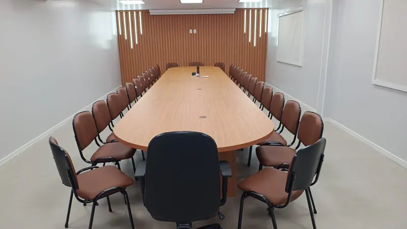 Sala de reuniões com mesa longa de madeira e painel ripado ao fundo